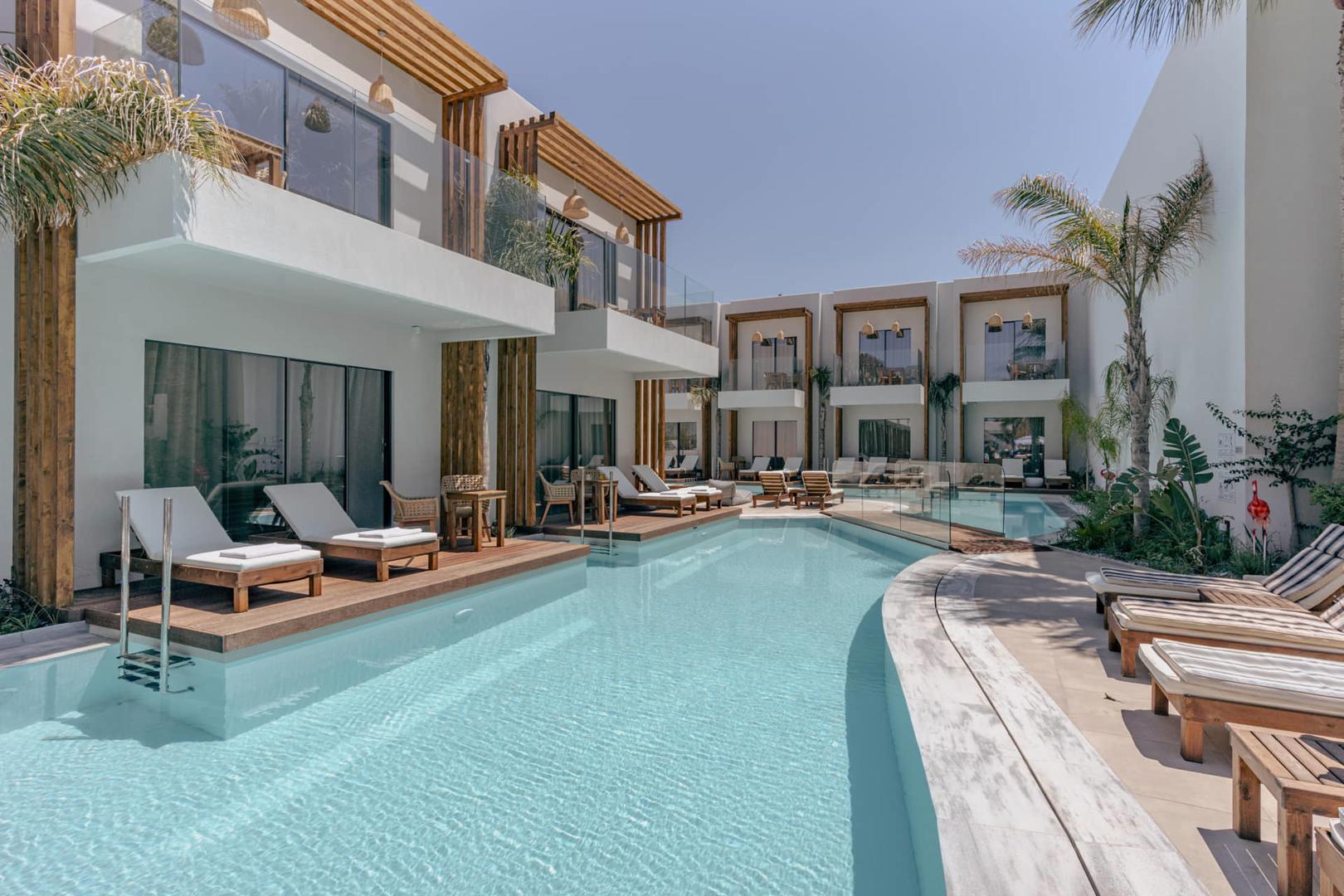 Lang zwembad met ligstoelen en kamers.